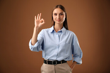 Beautiful woman showing okay gesture on brown background