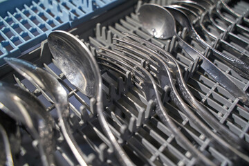 Close up of clean silverware in dishwasher rack focused on utensils and organization.