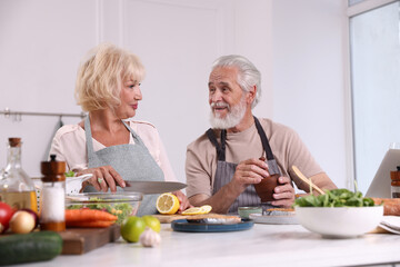 Elderly couple cooking together at table indoors