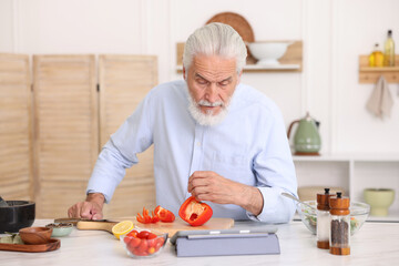 Elderly man using tablet while cooking at white marble table in kitchen