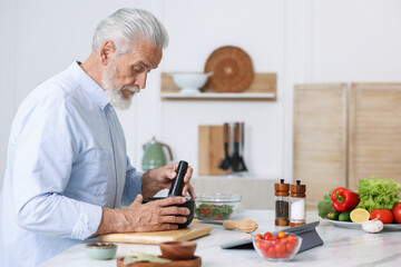 Elderly man cooking at white marble table in kitchen