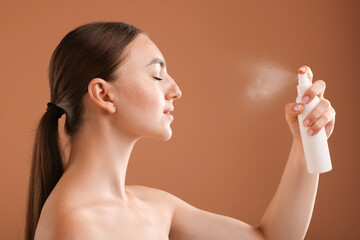 Beautiful woman spraying thermal water onto face on light brown background