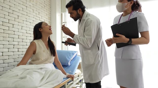 A physician performs an oropharyngeal examination on a patient, using a tongue depressor and penlight to assess for pharyngitis, tonsillitis, or other oral pathologies.