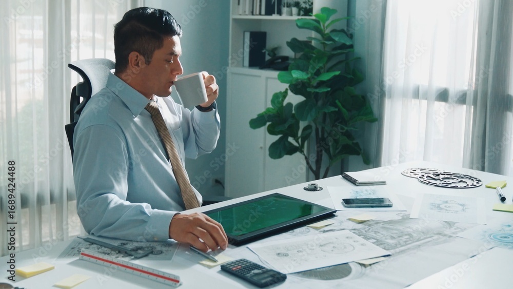 Poster professional engineer looking at phone while working on tablet with green screen at meeting table wi