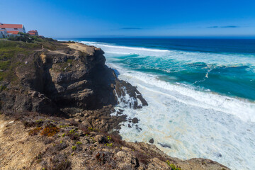 A dramatic coastal cliff overlooks powerful waves crashing against rocky shores