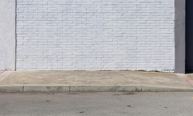 White painted brick wall at the roadside with concrete sidewalk and road in front. Background for copy space.