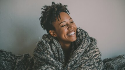 beautiful black woman sitting on couch wrapped under blanket and laughing cheerful african american woman relaxing at home carefree and happy mid lady hugging herself with warm blanket in winter no l