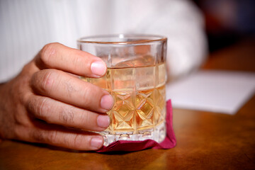 Businessman holding crystal glass of whiskey with ice on table