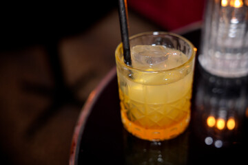 Refreshing yellow cocktail glowing on table in dark bar with ice and straw