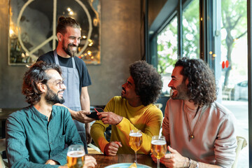 Young African American man paying for drinks with contactless technology in bar, enjoying time with friends.