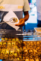Sweet street indulgence. 
A vendor serves a crunchy nut-covered pastry roll, traditional street dessert.