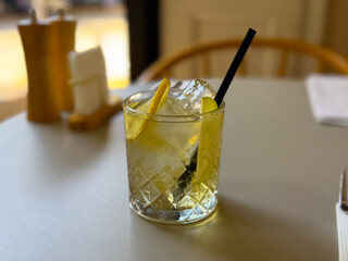 A glass of iced drink with lemon slices and straw stands on a cafe table. Refreshment, lifestyle,...