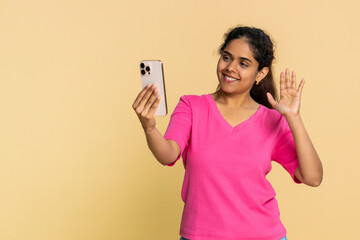 Naklejka premium Indian woman energetically waves, filming herself talking and smiling, recording an engaging video. Arabian girl expresses cheerful interaction, social media blogging, lively communication positivity