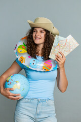 Woman tourist wearing inflatable ring around neck, holding globe and maps, recommending vacation at...