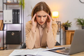 Middle-aged businesswoman at home office looks at bills invoices receipt on laptop sees costs go up...