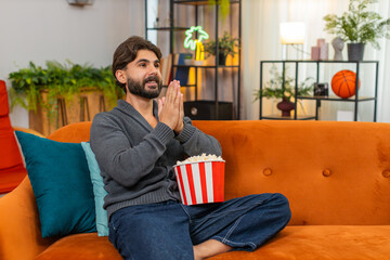Indian man at home watches series finale on TV holds popcorn tense pause then smiles and claps....