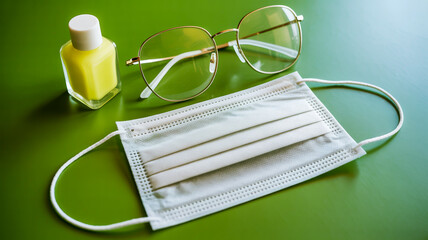 Medical face mask hand sanitizer and eyeglasses on green surface Keywords: face mask, hand sanitizer, eyeglasses, medical, health, hygiene, protection, safety