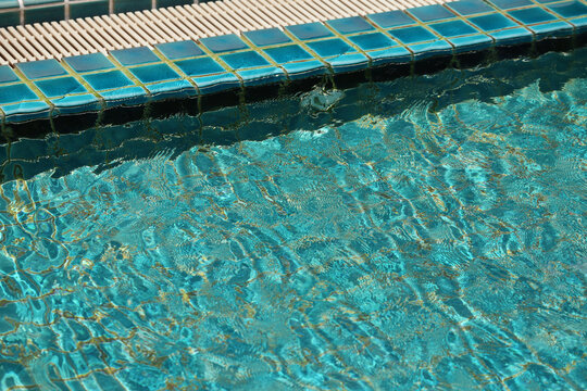 Edge pool with spillway grate. Pool with clear water is lined with blue-green tiles.