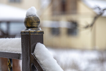 Close-up of a metal fence covered with fresh snow against a blurred countryside house. Winter rural...