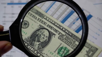 Finance professional scrutinizes us dollar bill through magnifying glass, analyzing investment performance against stock market graph, emphasizing detailed financial review - Powered by Adobe