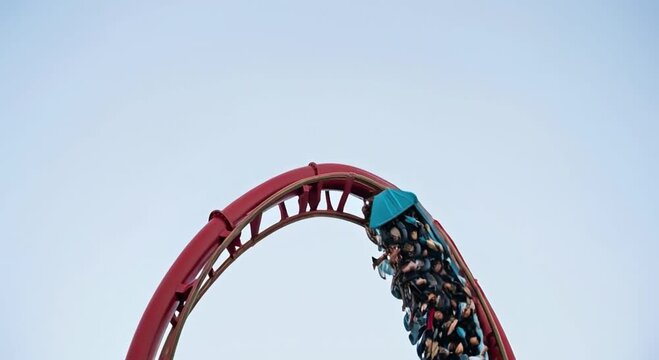 A red roller coaster track forms a thrilling loop high against a clear sky, carrying many excited passengers upside down on an exciting ride.