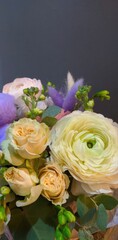 A beautiful bouquet with pastel ranunculus, roses flowers, and various green foliage. Natural floral arrangement for anniversary or gift. Vertical photo.