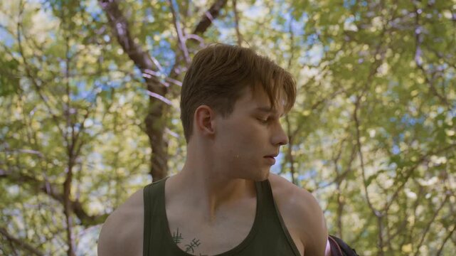 Young Soldier preparing for next stage of journey in the lonely forest, pulling off jacket and genuflecting, and picks up headband from black bag in readiness for the outdoor forest adventure