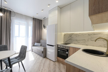 bright, modern studio apartment featuring a compact kitchen with white cabinets, marble backsplash, and a cozy living area with a small sofa and dining set