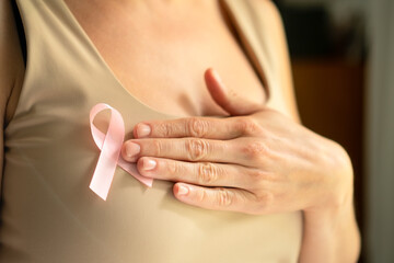 Close-up shot of female hand touching pink breast cancer awareness ribbon on shirt, symbolizing medical support and solidarity in October.