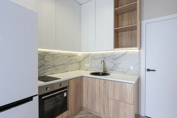 modern kitchen features white cabinets, a marble backsplash, light wood lower cabinets, and gold...