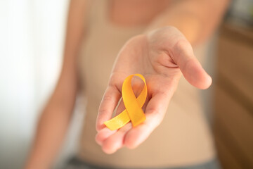 Detailed shot of yellow awareness ribbon resting on woman's open palm, representing solidarity with...
