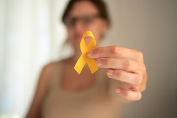 Close-up of female hand holding yellow satin ribbon, symbolizing support and awareness for children...