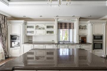 bright, elegant kitchen featuring ornate white cabinetry, dark countertops, and a large island. A...