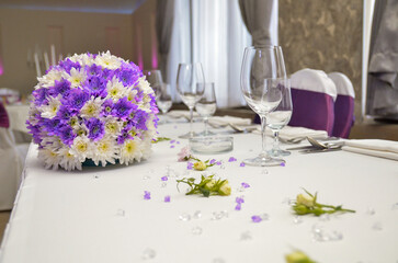 The wedding table decorated with three bouquets of purple and white flowers