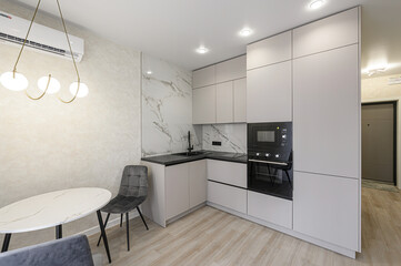 modern kitchen with gray cabinets, black countertops, and marble backsplash. There's a round table with gray chairs, and built-in appliances