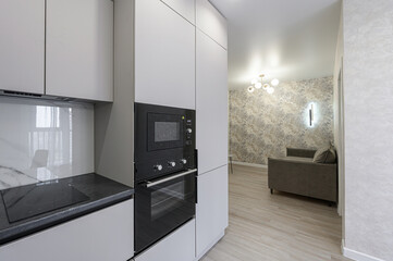 Modern kitchen and living area peek. Minimalist cabinets, built-in appliances. Stylish patterned wallpaper and soft lighting