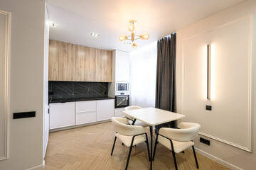 Modern kitchen featuring wooden cabinets, black marble backsplash, and white lower cabinets. A white table with four beige chairs sits in the foreground