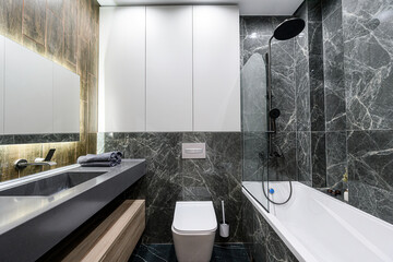 Modern bathroom with gray marble tiles, white cabinets, and dark fixtures. It features a sink,...