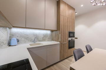 Modern kitchen with light grey cabinets, marble backsplash, wood-grain cabinet tower, and a bright countertop dining area