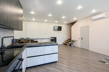 modern kitchen merges with the living area featuring gray cabinets, a black sink, a textured white wall, stairs, and light wood floors