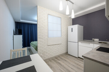 studio apartment with a kitchen area featuring a white refrigerator, brick wall, and a glimpse of a bedroom space