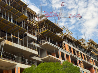 Fototapeta premium Brick walls and scaffolding at a construction site with a crane above. Architectural growth, structural engineering and urban expansion.