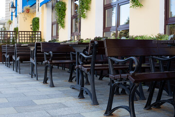Peaceful outdoor cafe scene with benches and tables under the shade, creating perfect space for relaxation. Neat arrangement and surrounding greenery invite guests to enjoy urban dining