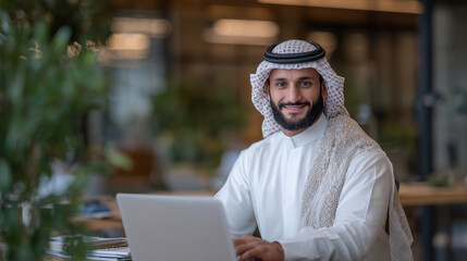 Focused Arab professional in traditional clothing seated at office desk, smiling while interacting with laptop, stylish workspace with motivational vibe