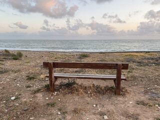 A Serene Seaside View Featuring an Empty Wooden Bench Overlooking the Calm Ocean and Soft Clouds at Dusk