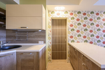 modern kitchen with light beige cabinets, a countertop, and a door. The walls feature a colorful floral wallpaper