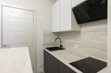 modern kitchen with white cabinets, gray countertops, and black appliances. White brick walls and a white door add texture to the space