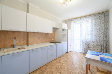 bright kitchen features white upper cabinets, light blue lower cabinets, and a floral curtained window. A table stands to the right