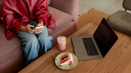 A person sits with a laptop, cake, and a drink in a cozy cafe setting, working.