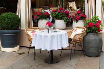 Cozy outdoor cafe setting with a white tablecloth, wicker chairs, wine glasses, and vibrant pink hydrangeas creating a romantic ambiance.